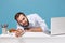 Tired perplexed young man in shirt sit work at desk with pc laptop isolated on blue background. Achievement business