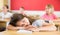 Tired preteen girl sleeping at desk at lesson in classroom