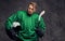 Tired professional hockey player in a green sportswear holds a hockey stick and protective helmet on a gray background.