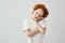 Tired red haired boy with freckles in white t-shirt looking aside with relaxed expression, holding head with hand.