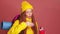 Tired redhaired ginger woman in pink studio background wearing yellow windbreaker jacket with hat and holding on her