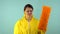 Tired and Sad Cleaning Lady in a Yellow Suit and Gloves with a Broom in Hands on a Blue Background. Cleaning Concept