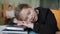 Tired schoolgirl sleeping on desk in classroom. Portrait of exhausted Caucasian learner with head on books in public