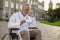 Tired senior handicapped male doctor in wheelchair wearing lab coat taking off his glasses, having headache, posing