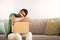 Tired serious pensive young middle eastern guy blogger resting on cardboard box, sits on sofa