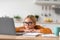 Tired serious pretty european teenage girl pupil in glasses looks at laptop, sits at table