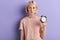 Tired sleepy serious woman holding alarm clock isolated over violet background