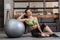 Tired sportswoman sitting near fitness ball at home and