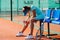 Tired teenage girl sitting on a chair bench next to tennis court to take a short break