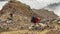 A tired tourist with a large backpack stumbles along a mountain path past stones and boulders.