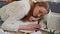 Tired woman at home office falling asleep on table with laptop computer, crumpled sheets of paper