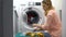 Tired woman loading clothes in washing machine, annoyed with housework routine