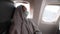 tired woman passenger in covid safety face mask sleeping in seat at window in airplane