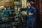 A tired worker in a blue protective suit is standing by a turning machine. Portrait of a turning fitter.