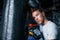 Tired young boxer in white shirt and with protective gloves leaning on punching bag in the gym