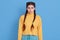 Tired young dark haired woman purses lips, feels sadness, wearing yellow jumper, isolated over blue background, being upset,