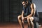 Tired young sportsman with towel on neck sitting on barbell