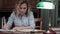 Tired young woman finishing her report, closing the book, turning the lamp off and leaving her desk