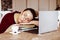 Tired young woman in glasses sleeping on books near laptop at desk in home room. Tiredness from monotonous study and