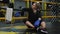 A tired young woman sits in a boxing ring after a workout and drinks water.