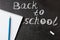 Title Back to school written by white chalk and the the notebook with blue pencil on the black school chalkboard