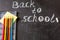 Title Back to school written by white chalk and the the notebook with colorful pencils on the black school chalkboard