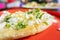 Tlacoyo with cheese, green sauce, and sour cream on a red plate