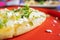 Tlacoyo with cheese, green sauce, and sour cream on a red plate