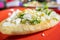 Tlacoyo with cheese, green sauce, and sour cream on a red plate