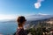 Toarmina - Tourist woman with panoramic view on snow capped Mount Etna and the Mediterranean sea from Taormina, Sicily, Italy