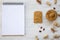 Toast, bowl of peanut butter, peanuts and notebook on a white wooden background, top view.