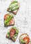 Toast sandwiches with avocado, salami, asparagus, tomatoes and soft cheese on light background, top view. Tasty breakfast, snack o