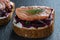 Toast from a slice of bread with white cream cheese, stewed beetroot pulp,salmon fillets, seeds and green dill on wooden board.