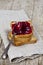 Toasted cereal bread slices stack with homemade cherry jam and spoon closeup on rustic wooden table background