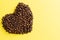 Toasted coffee beans in heart shape on yellow background