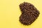 Toasted coffee beans in heart shape on yellow background