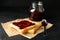 Toasts and glass jar with jam, spoon and baking paper on background, close up