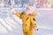 Toddler 12-17 months old in yellow winter clothes looks at falling snowflakes while walking in a winter park