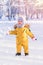 Toddler 12-17 months old in yellow winter clothes rejoices in the fallen snow while walking in the winter park