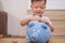 Toddler baby boy child putting Thai coin into blue piggy bank