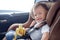 Toddler baby boy child sitting in safety carseat holding & enjoy eating banana