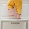 Toddler baby boy climbed with his feet on a high chair to climb on the kitchen cabinet. Child safety issues in the home room,