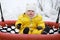 Toddler baby boy in a yellow snowsuit is swinging on a swing in a snow