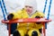 Toddler baby boy in a yellow snowsuit is swinging on a swing in a snow