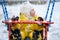 Toddler baby boy in a yellow snowsuit is swinging on a swing in a snow