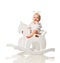 Toddler baby girl is riding swinging on a rocking chair toy horse over white