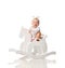 Toddler baby girl is riding swinging on a rocking chair toy horse over white