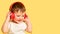 Toddler baby listens to music in red headphones on a studio yellow ba