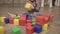 toddler baby sits wooden floor gray pajamas plays multi-colored plastic cubes