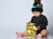 Toddler in black bodysuit and hat with croco print, barefoot. He holding gift, sitting on floor isolated on white. Close up